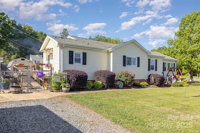ranch-style home featuring a playground, a front lawn, a shed, roof with shingles, and an outdoor structure