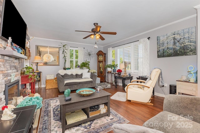 living room with crown molding, a ceiling fan, baseboards, wood finished floors, and a fireplace