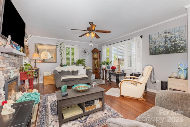 living area featuring ornamental molding, a ceiling fan, a stone fireplace, baseboards, and wood finished floors