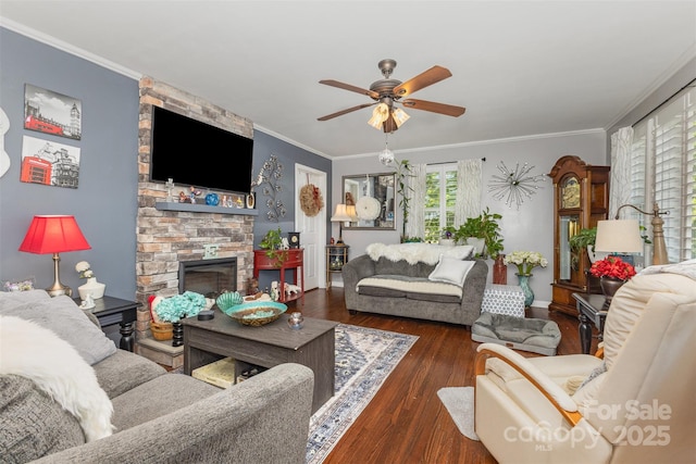 living room featuring ceiling fan, wood finished floors, a stone fireplace, crown molding, and baseboards