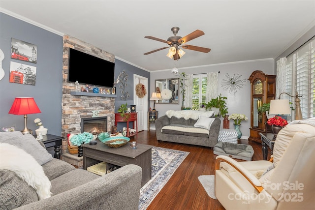 living room with a ceiling fan, wood finished floors, a stone fireplace, ornamental molding, and baseboards