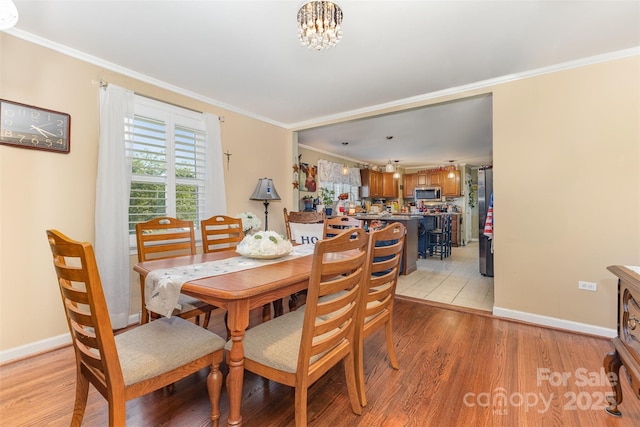 dining area with light wood finished floors, ornamental molding, a chandelier, and baseboards