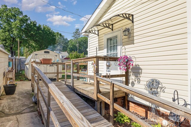 wooden terrace featuring a shed, fence, and an outbuilding