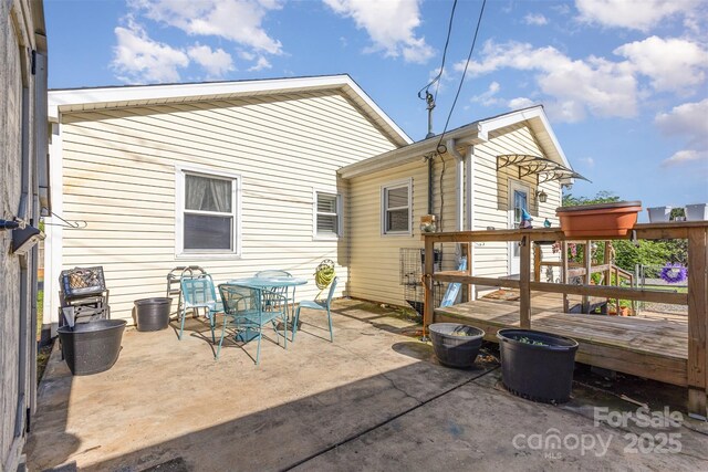 back of house with a wooden deck, outdoor dining space, and a patio