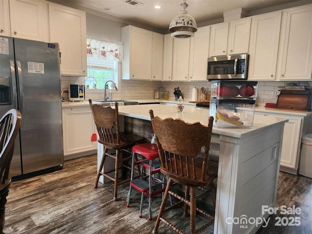 kitchen with white cabinets, appliances with stainless steel finishes, light countertops, dark wood finished floors, and a center island