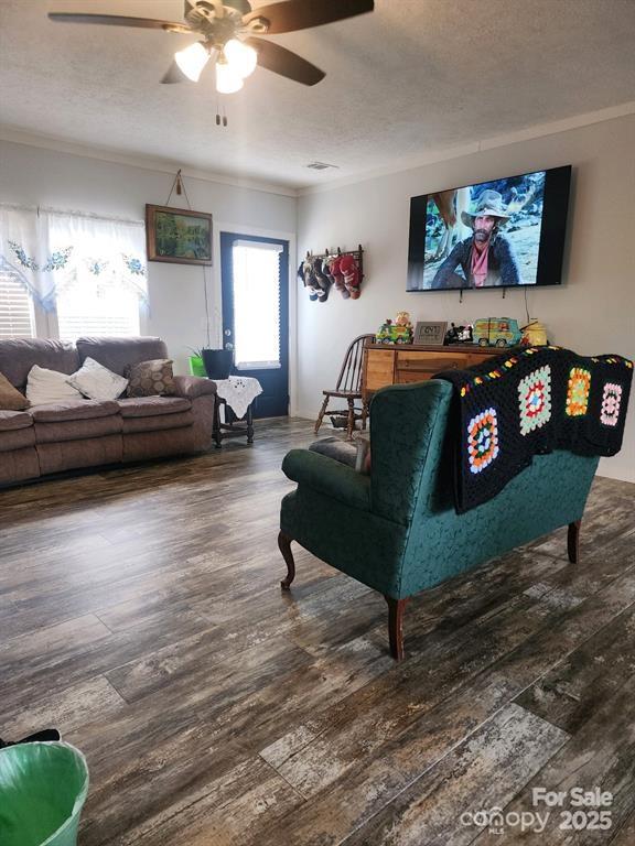 living room featuring ornamental molding, a textured ceiling, ceiling fan, and wood finished floors