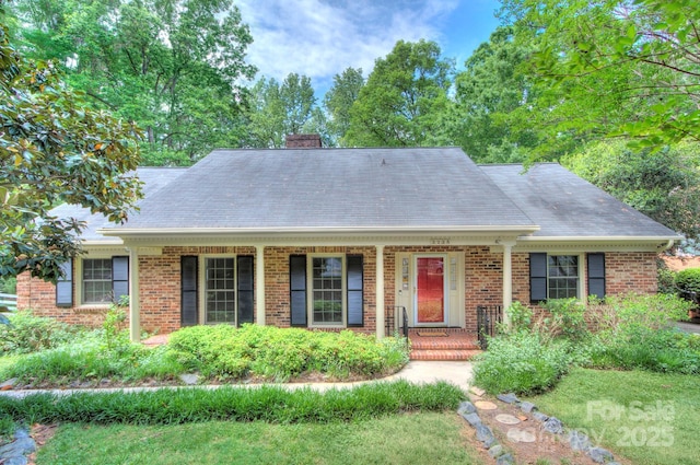 ranch-style home featuring roof with shingles, covered porch, a chimney, and brick siding