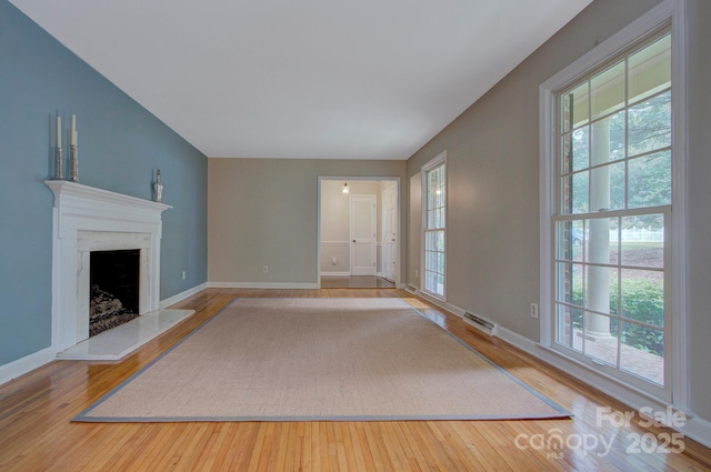 unfurnished living room featuring a fireplace with raised hearth, baseboards, visible vents, and wood finished floors