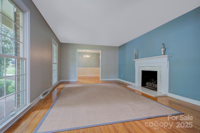 unfurnished living room with baseboards, a notable chandelier, wood finished floors, and visible vents