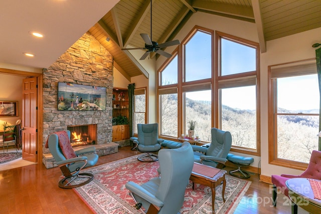 living room with wooden ceiling, hardwood / wood-style floors, beam ceiling, a fireplace, and a ceiling fan
