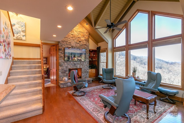 living room with hardwood / wood-style flooring, a ceiling fan, a stone fireplace, stairway, and beamed ceiling