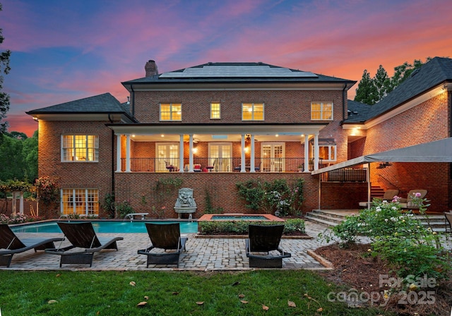 3314 Leamington Ln, Charlotte, NC 28226 - back of house at dusk with a patio area, solar panels, brick siding, a chimney, and an in-ground hot tub