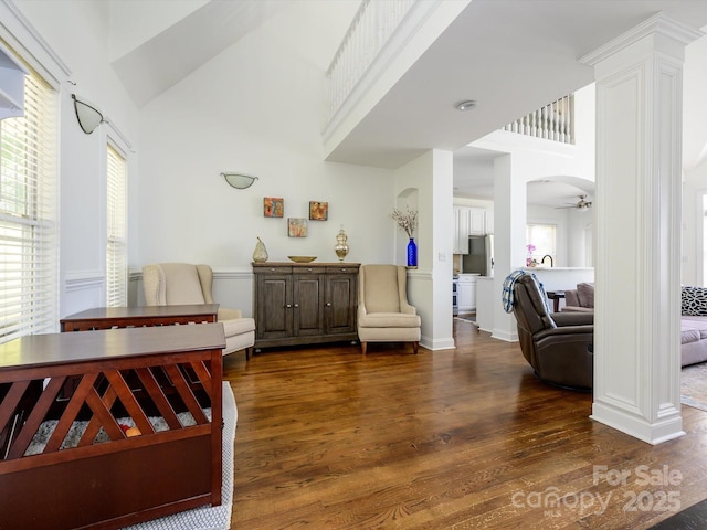 sitting room featuring a ceiling fan, dark wood-style flooring, ornate columns, and a high ceiling