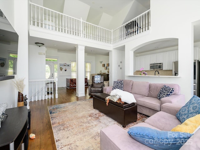 living area with wood finished floors, a towering ceiling, and ornate columns