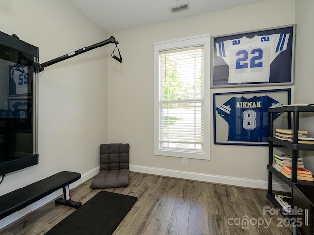 exercise room with baseboards, visible vents, and wood finished floors