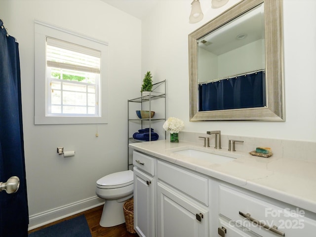 bathroom featuring toilet, baseboards, wood finished floors, and vanity