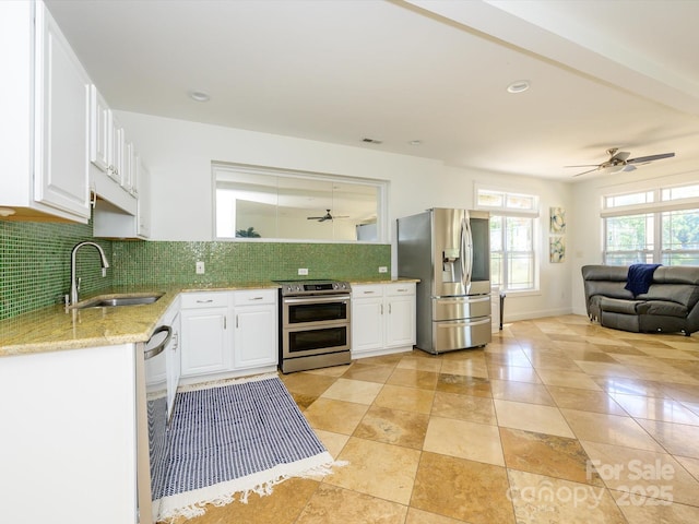 kitchen featuring a ceiling fan, a sink, open floor plan, backsplash, and appliances with stainless steel finishes