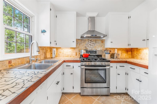 kitchen featuring stainless steel gas range oven, a sink, white cabinetry, wall chimney exhaust hood, and light countertops