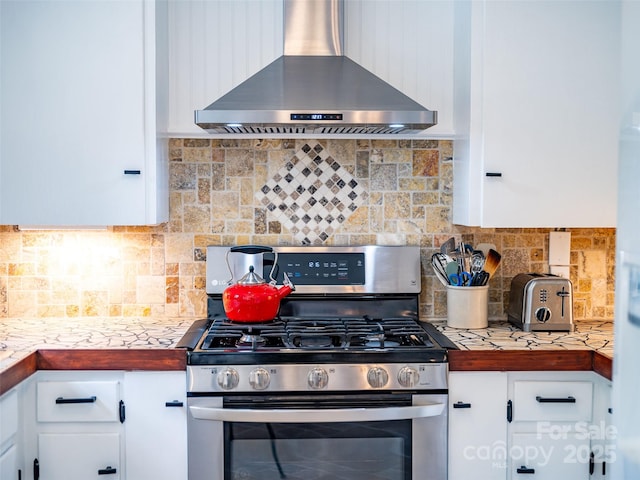 kitchen with white cabinets, wall chimney range hood, stainless steel gas stove, and backsplash