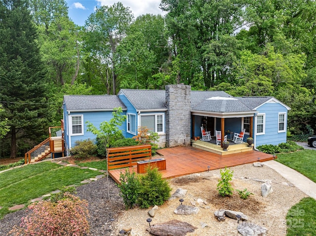 rear view of house featuring a lawn, a chimney, a wooden deck, and roof with shingles