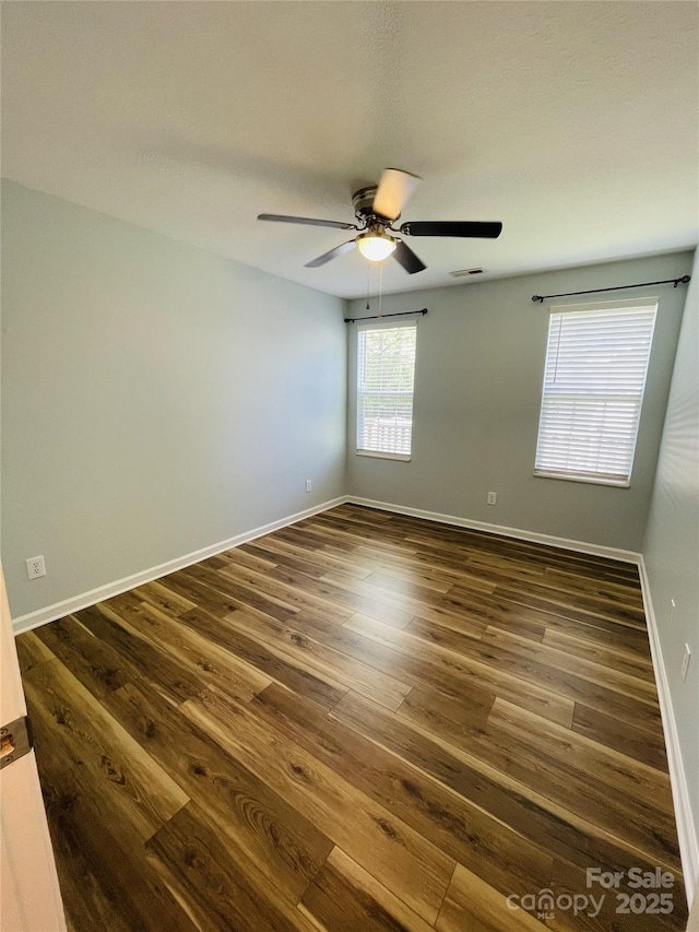 spare room featuring visible vents, baseboards, ceiling fan, and dark wood-style floors