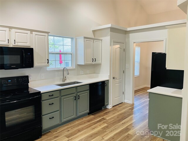 kitchen featuring a towering ceiling, light wood-style floors, white cabinets, a sink, and black appliances