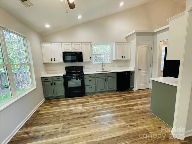 kitchen with vaulted ceiling, light wood-type flooring, a sink, green cabinets, and black appliances