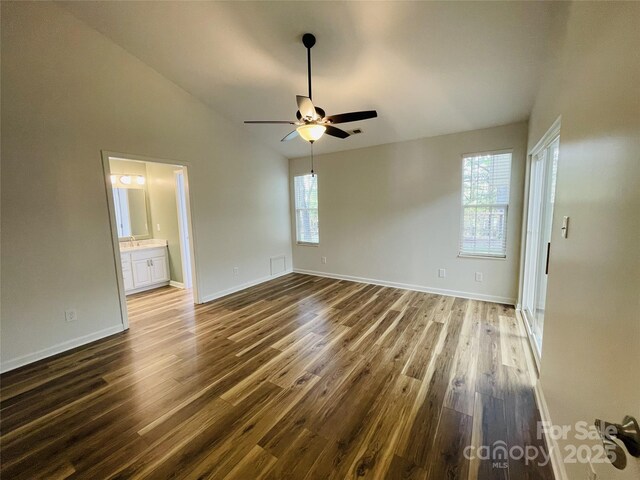 interior space with baseboards, lofted ceiling, connected bathroom, and dark wood-type flooring