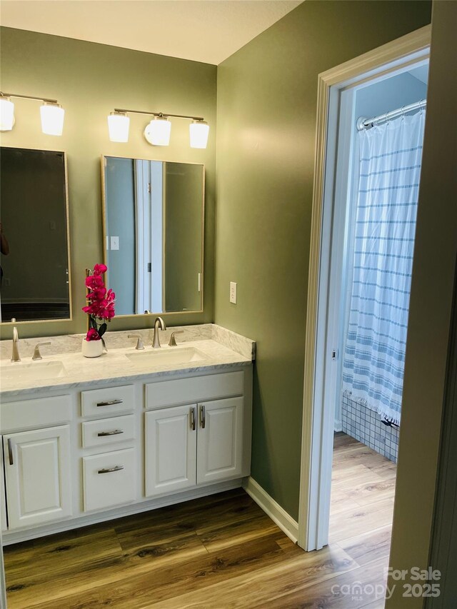 bathroom with double vanity, a sink, baseboards, and wood finished floors