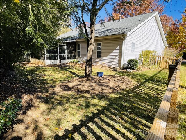 back of property with a sunroom, roof with shingles, a lawn, and fence
