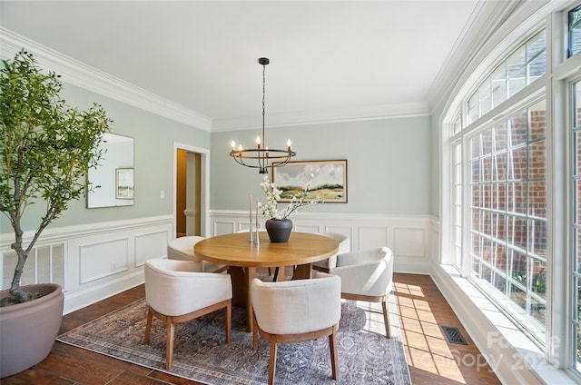 dining area featuring a wainscoted wall, ornamental molding, dark wood finished floors, and a notable chandelier