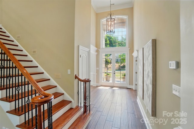 entryway with a towering ceiling, wood finished floors, stairway, french doors, and a notable chandelier