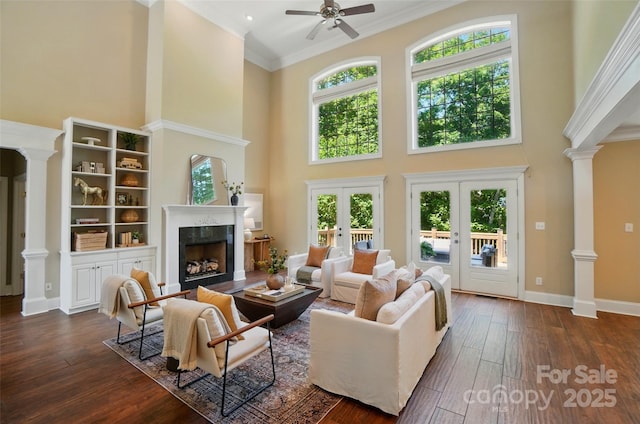 living room featuring a healthy amount of sunlight, decorative columns, dark wood-style floors, a high ceiling, and a premium fireplace