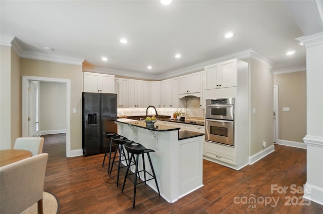 kitchen featuring a kitchen island with sink, dark countertops, a kitchen breakfast bar, tasteful backsplash, and black appliances