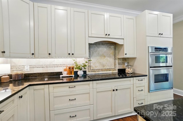 kitchen with stainless steel double oven, tasteful backsplash, black electric cooktop, dark stone countertops, and white cabinetry