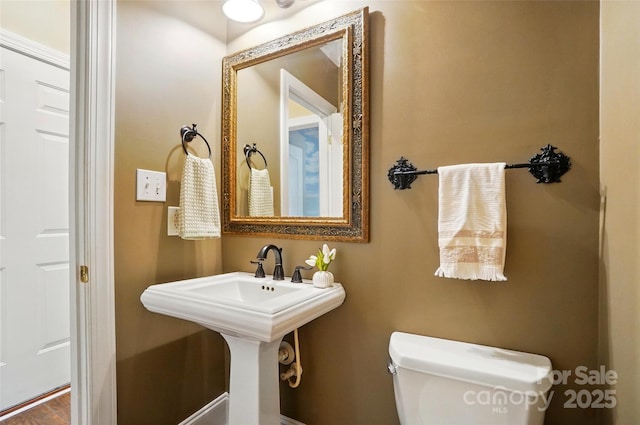half bath with toilet, baseboards, and a sink