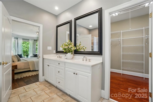 ensuite bathroom with double vanity, wood finished floors, baseboards, a sink, and ensuite bath