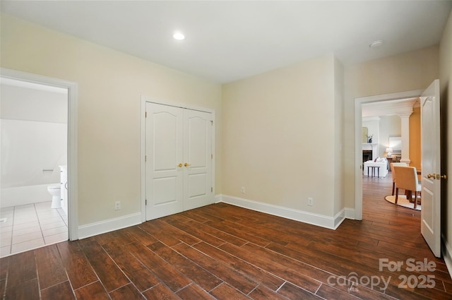 unfurnished bedroom featuring baseboards, dark wood finished floors, ensuite bathroom, and a closet