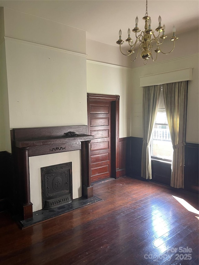 unfurnished living room featuring a fireplace, a chandelier, wainscoting, and wood finished floors
