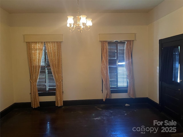 unfurnished room featuring an inviting chandelier, wood finished floors, and baseboards