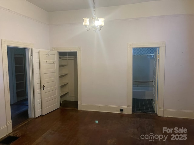 unfurnished bedroom with a chandelier, wood finished floors, baseboards, a closet, and a walk in closet