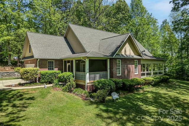view of front of property featuring a shingled roof, a sunroom, a front yard, and brick siding