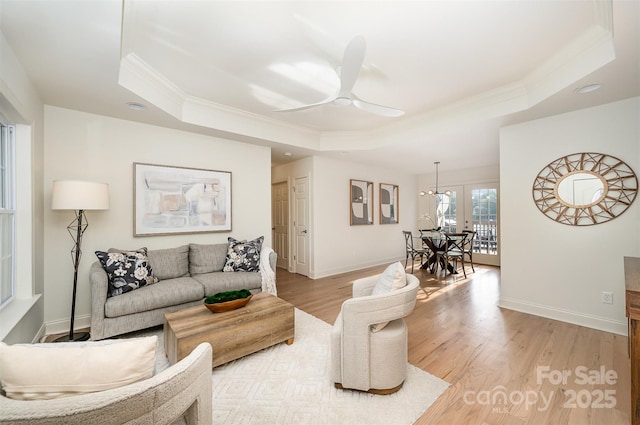 living room featuring ceiling fan with notable chandelier, baseboards, light wood-type flooring, a tray ceiling, and ornamental molding