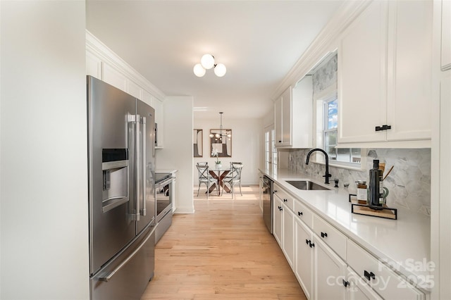 kitchen featuring backsplash, appliances with stainless steel finishes, a sink, light wood finished floors, and white cabinetry