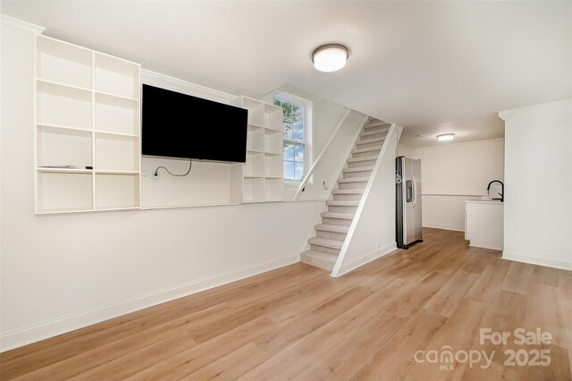 below grade area featuring stainless steel refrigerator with ice dispenser, baseboards, light wood finished floors, and stairs