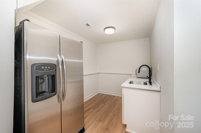 kitchen featuring visible vents, light wood-type flooring, a sink, baseboards, and stainless steel fridge