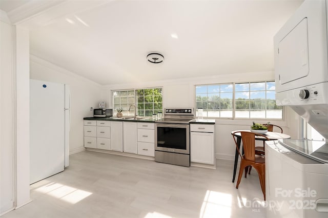 kitchen with stacked washer and dryer, stainless steel electric range, white cabinets, freestanding refrigerator, and lofted ceiling