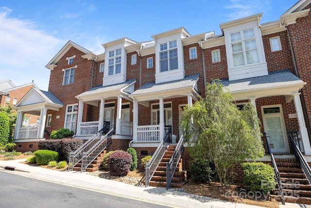 multi unit property with covered porch, brick siding, and stairway