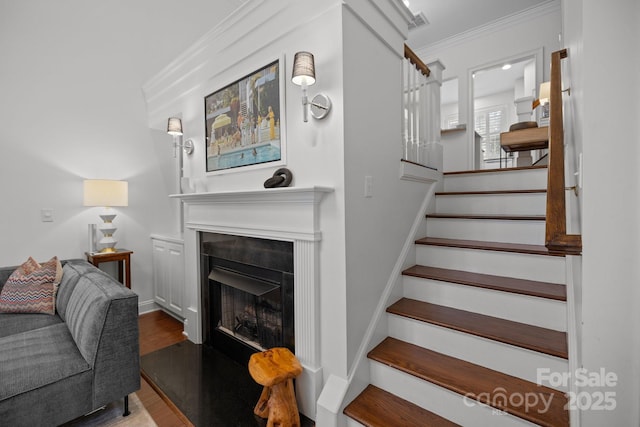 staircase with crown molding, wood finished floors, and a fireplace