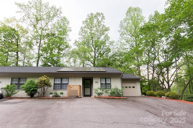 ranch-style home featuring a garage, board and batten siding, aphalt driveway, and solar panels